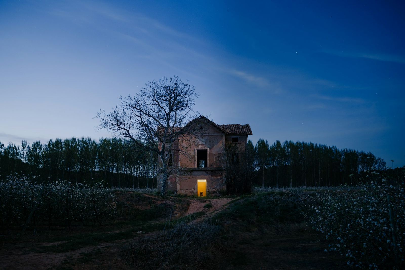 A lone brick house with one lit window at dusk